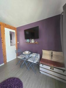 a room with a purple wall with a table and a tv at Chambre double "le pêcher" saillans in Saillans