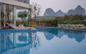 a building with a swimming pool with mountains in the background at Xitang River View Holiday Motel in Yangshuo
