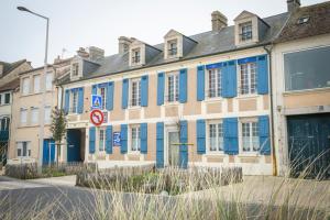 a building with blue shutters on a street at Maison Studios & Appartements Les 4 Vents in Luc-sur-Mer