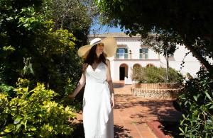 a woman in a white dress and hat standing in front of a house at Isola Charm B&B - Pool & Nature Stay in Syracuse +84 photos