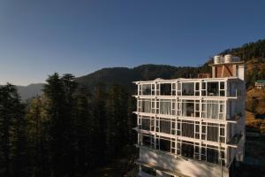 a white building with trees and mountains in the background at White Castle Himalayan View by Lavender Hotels in Shimla