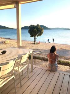 a woman sitting on a deck looking at the beach at BUQEZ Eco Resort - beachfront 20 & House 42 in Drage