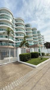 a large white building with palm trees in front of it at Apart completo RESORT Pé na Areia RECREIO in Rio de Janeiro