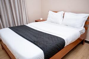 Una cama con sábanas blancas y una manta negra. en 1 Bedroom Apartment in Kampala - WiFi - PowerBack - Workspace, en Kampala