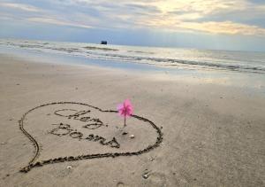 ein Herz im Sand mit einer rosa Blume in der Unterkunft Caprices des vagues - A 300 m de la plage et à 4 kilomètres de Nausicaa, Place de parking privée, Eau douce, Netflix, Primes Vidéo, Wifi haut débit in Le Portel
