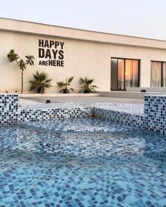 una piscina frente a un edificio con un cartel que lee días felices están aquí en Blanca house with 2pools near Sharjah Al Dhaid, en á¸¨aÅŸat al BidÄ«yah