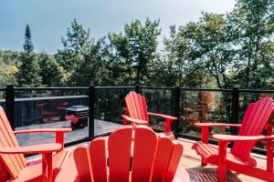 three red chairs sitting on a deck with trees at Le Yéti de Tremblant in La Conception