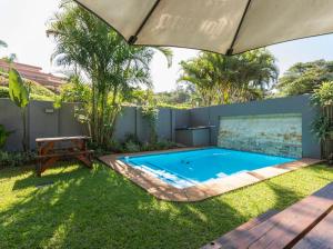 a swimming pool in a yard with an umbrella at Eden Palms , Ballito in Shakaʼs Rock