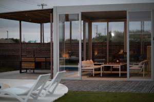 a patio with white chairs and a table and glass doors at VILLA Seamu 九十九里 家族と愛犬で楽しむサウナとプール ガラス貼りBBQルーム付き高級ガーデンヴィラ in Kujukuri