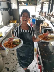 una mujer en una cocina sosteniendo dos platos de comida en Bar Ang Guesthouse, en Battambang