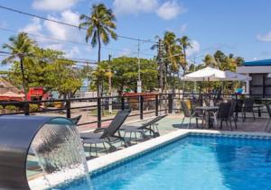 a swimming pool with chairs and a table and an umbrella at Flat luxury hotel cove in Maceió