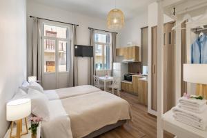 a white bedroom with a bed and a kitchen at Irene Studios in Ermoupoli