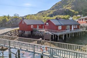 a group of red buildings on the water with a dock at Fisherman's cabin, Lofoten - Brattelibua in Ballstad +13 photos