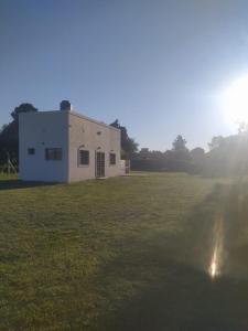 un edificio bianco in un campo con il sole sullo sfondo di El Quincho de Ampi a Chascomús