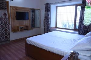 ein Schlafzimmer mit einem Bett, einem Fernseher und einem Fenster in der Unterkunft Rooptara Valley Luxury Cottage Majkhali Himalaya in Rānīkhet