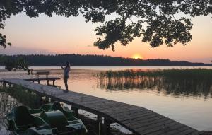 une femme debout sur un quai près de l'eau au coucher du soleil dans l'établissement Lovely Home In Swietajno With Kitchen, à Świętajno