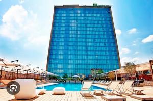a large glass building with chairs and a pool at Cozy Apartment Near Holiday Inn in Tbilisi City