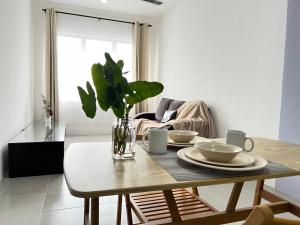 a dining room table with plates and a vase with a plant at N&N Modern Apartment in Kampong Padang Meha