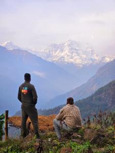dos hombres sentados en una colina mirando una montaña en Chaukhamba Cradle, en Ukhimath