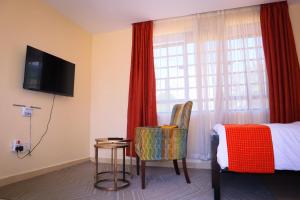 a hotel room with a bed and a chair and a television at 3 Jays Homes in Narok