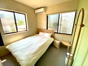 ein kleines Schlafzimmer mit einem Bett und zwei Fenstern in der Unterkunft SANDBoX in Oshima
