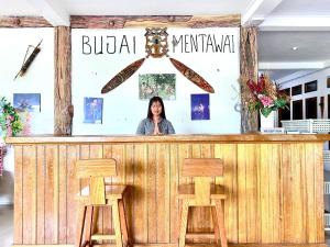 a woman standing behind a bar with two wooden stools at Bujai Mentawai Griya Hotel in Tuapejat