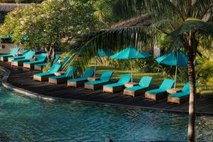 a row of blue lounge chairs and umbrellas next to a pool at Vila Ombak in Gili Trawangan