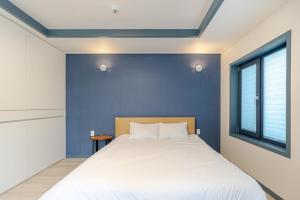Un dormitorio con una cama blanca y una pared azul. en Jeju Aewol Sugar Pension, en Jeju