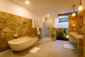 a bathroom with a large tub and a stone wall at Vila Ombak in Gili Trawangan