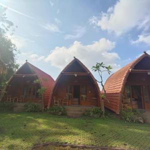 a group of three huts in the grass at WArDiTa Paddy Lodge in Labuhanamuk