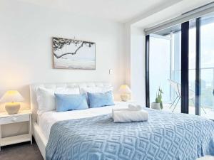 a white bedroom with a large bed with blue pillows at Amazing SeaView Central Stylish Near Aotea Square in Auckland