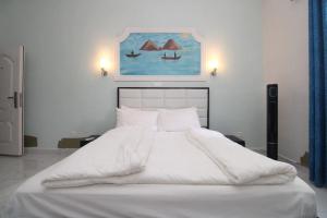 a bedroom with a white bed with a painting on the wall at Afriqpnb RAP Studio 102 avec Piscine in Douala