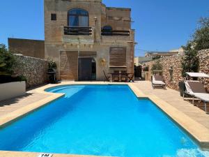 a swimming pool in front of a building with a house at Villa farmhouse with large private pool Gozo in Qala