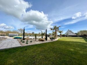 a yard with palm trees and a grass field at Superbe Villa tout confort avec piscine chauffée er couverte et spa à 2 pas de la plage in Fouesnant