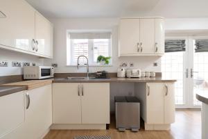 a kitchen with white cabinets and a sink at The Romford Oasis - Spacious 4 bedroom escape in Havering atte Bower
