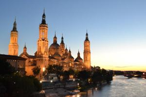 a large building with towers and a river at dusk at Apartamenticos Living San Pablo in Zaragoza
