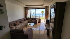 a living room with a couch and a table and a television at Appartement Plage des Nations Prestigia Front Mer avec grand Jardin in Sidi Bouqnadel