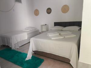two beds in a white room with a green rug at Residencial Girassol Outeiro in Porto Seguro