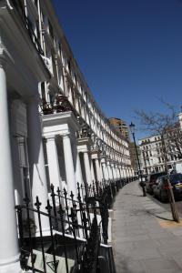 a building with white columns and a fence next to a sidewalk at Exhibition Court Hotel 4 in London