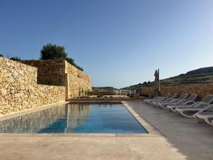 a swimming pool with chairs and a stone wall at Veduta Ta Pinu Apartments with Stunning Views Garden Sauna Pool and Gym in Għarb