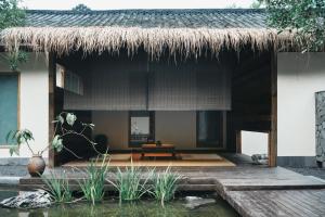 a house with a thatched roof and a pond at YunXi ChanYi Forest Soup Spring Resort Hotel ,Provides pick-up service and tea leaves,Drink Chinese wild tea leaves in Emeishan City