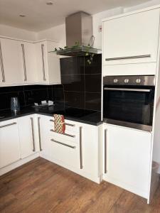 eine Küche mit weißen Schränken und schwarzen Geräten in der Unterkunft Modern 3 Bed Free Parking 10 mins walk to station in Dagenham