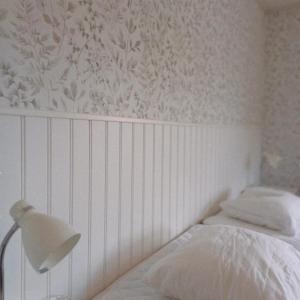 a white bedroom with a bed and a lamp at Borrgården Hostel in Ljusdal