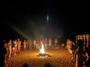 un grupo de personas de pie alrededor de un fuego en una playa en Desert shine camp, en Wadi Rum