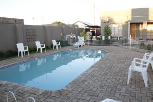 ein kleiner Pool mit weißen Stühlen und einem Zaun in der Unterkunft Asante Apartments in Livingstone