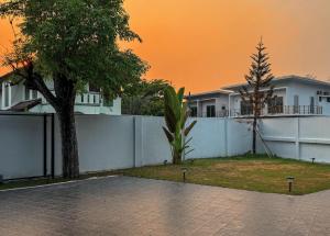 a white fence with a tree in front of a house at 提供免费汽车使用的含泳池被墅房间 in Chiang Mai