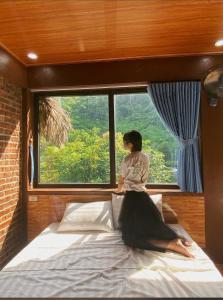 a woman sitting on a bed in front of a window at Tam Coc Moutainside Homestay in Ninh Binh
