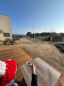 a person holding a cup of coffee on a deck at Camping de l'Espérance - Camping Côte de granit rose - Trébeurden - Ile grande - GR34 in Trébeurden