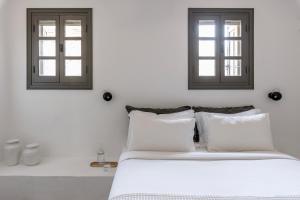 a white bedroom with two windows and a bed at Acron Villas Paros in Kolympithres