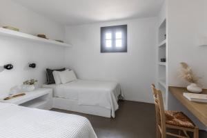 a white bedroom with a bed and a desk with a chair at Acron Villas Paros in Kolympithres